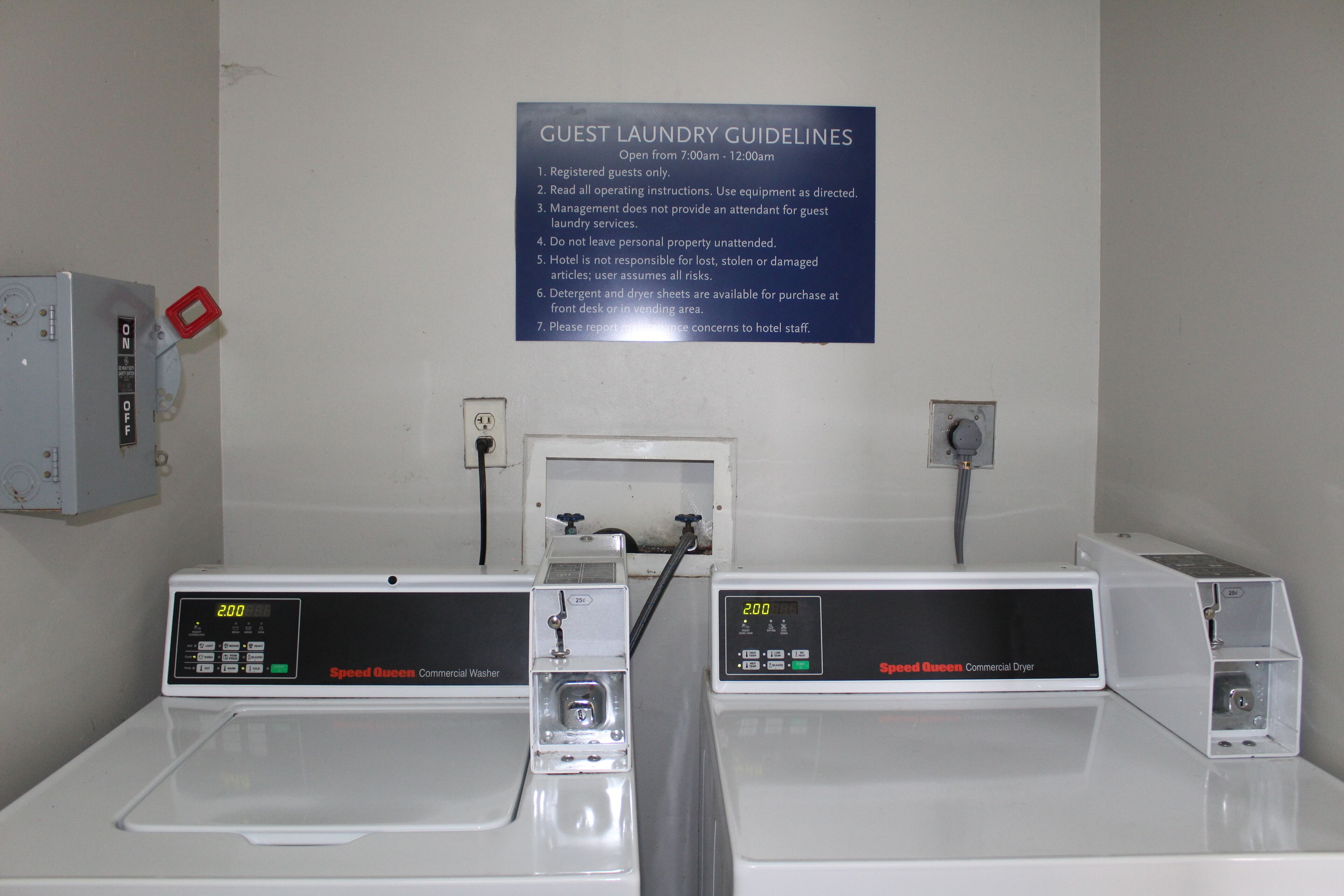 A hotel laundry area with Speed Queen commercial washers and dryers, a guest laundry guideline sign, and a control panel with a digital display.