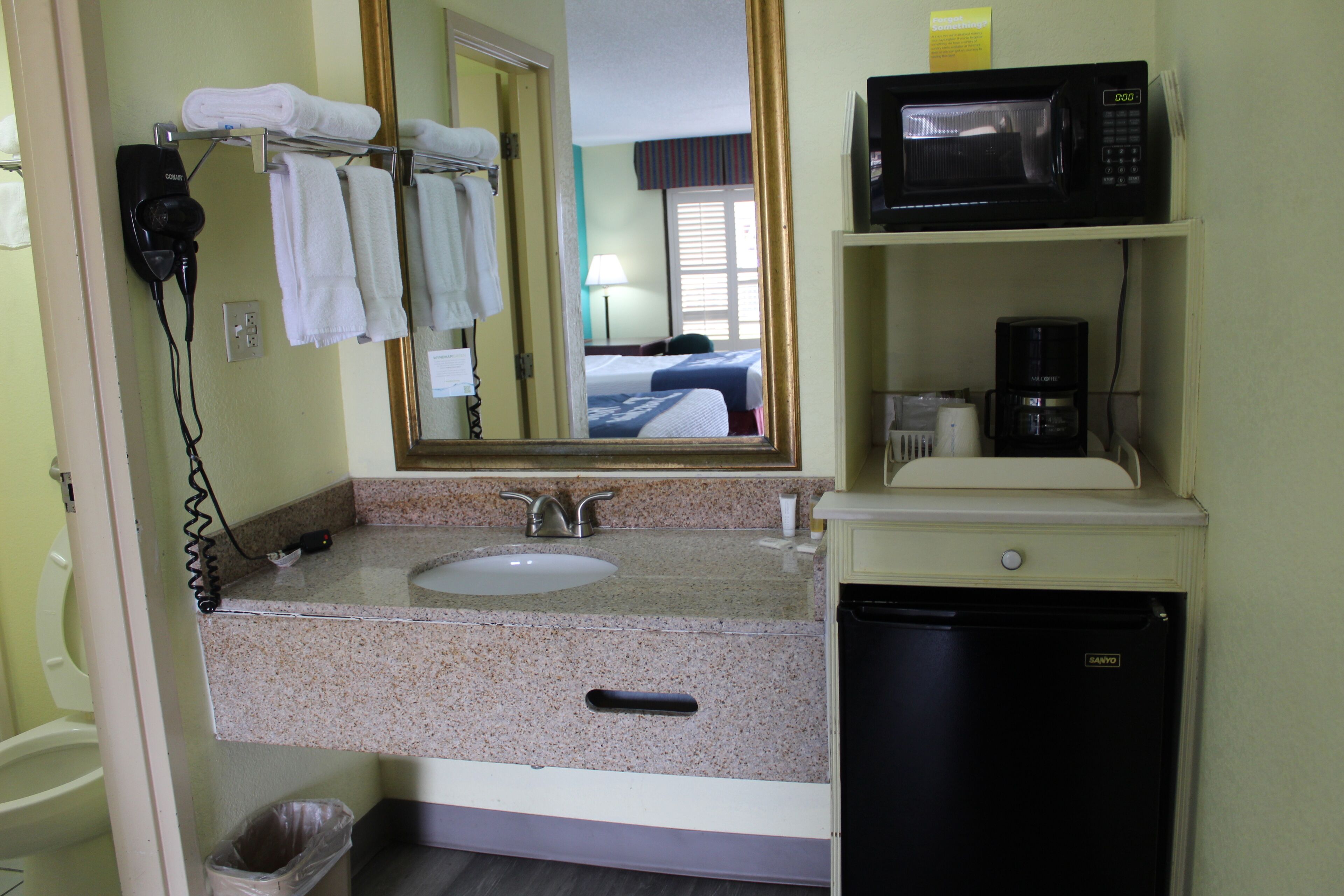 A bathroom with a sink, mirror, hair dryer, towels, a microwave, and a coffee maker.