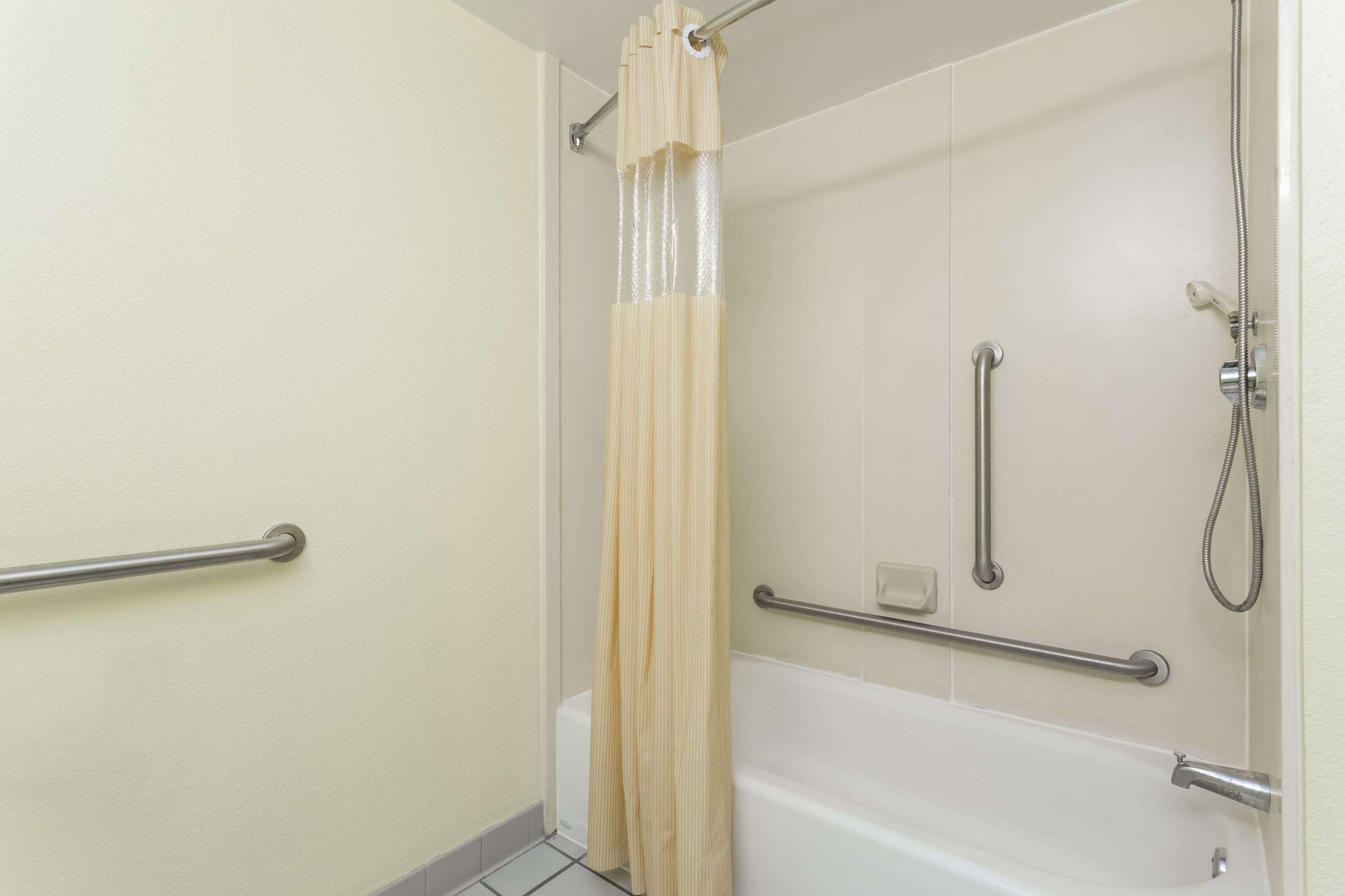 A bathroom with a bathtub, a shower, and a toilet. There are grab bars installed for safety.