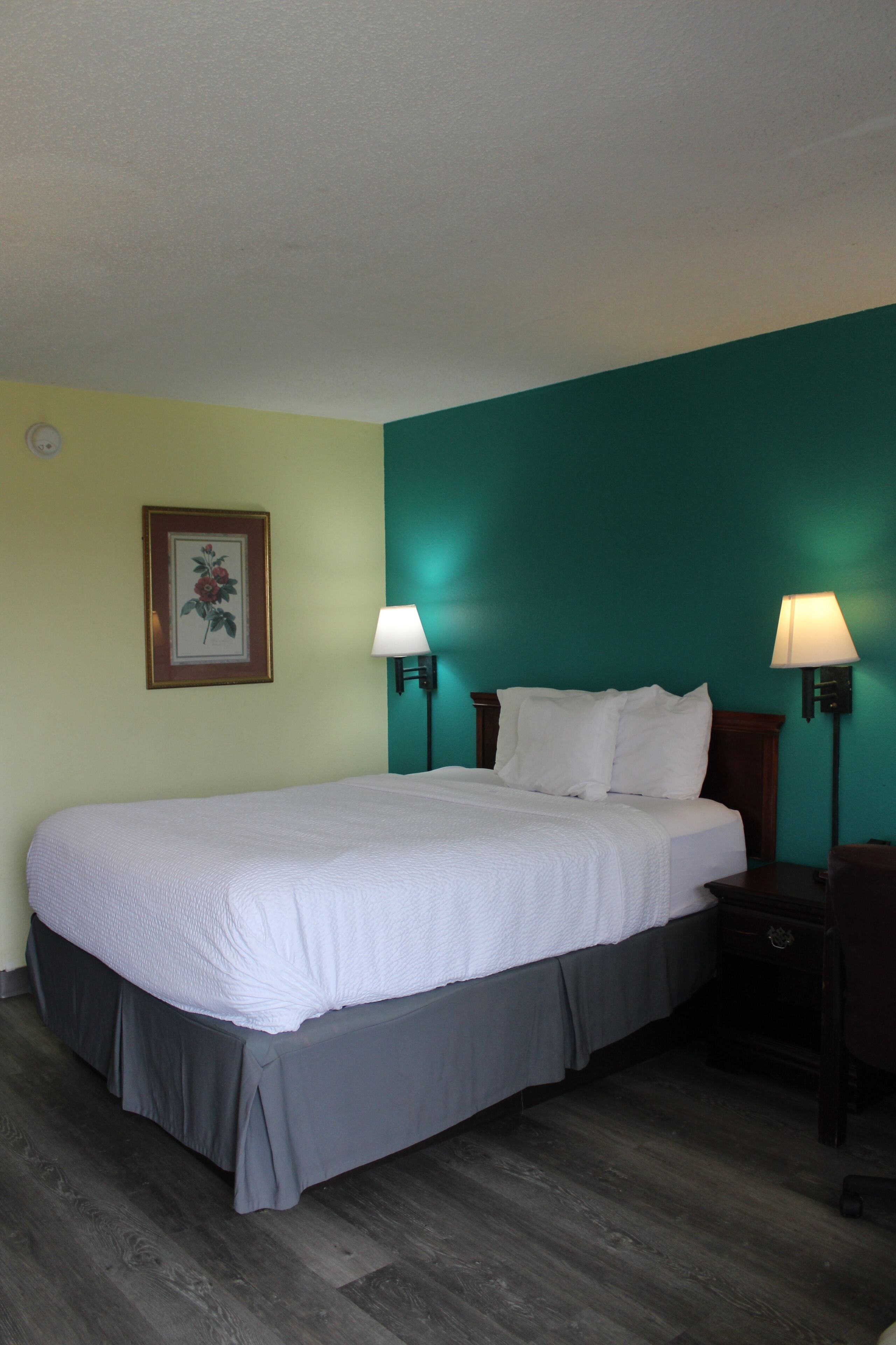 A hotel room with a large bed, two bedside lamps, a framed picture on the wall, and a teal accent wall.