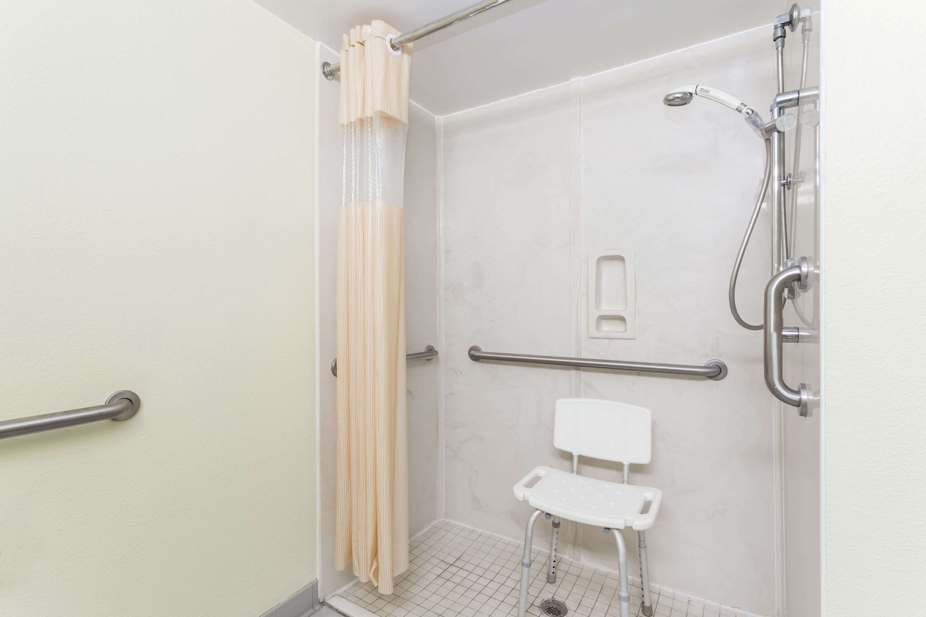 A bathroom with a shower, grab bars, a white toilet, and a safety shower seat.