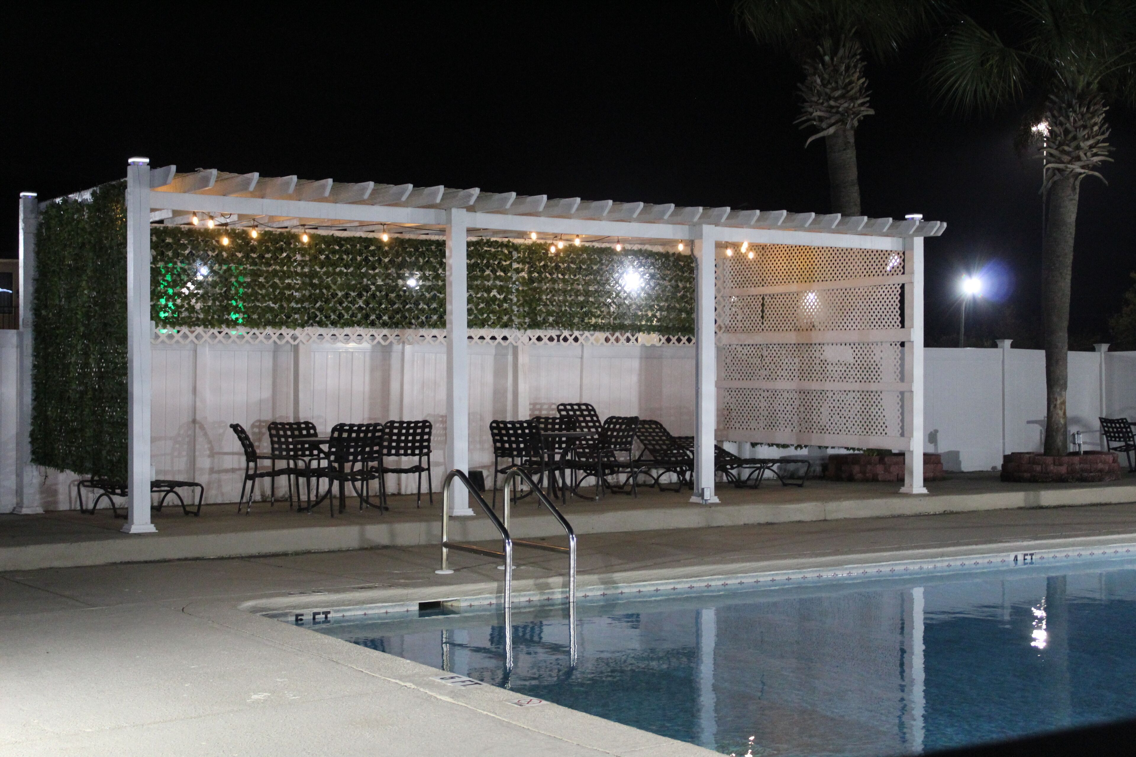 A pool area with a covered seating area, chairs, and a pool with a ladder.