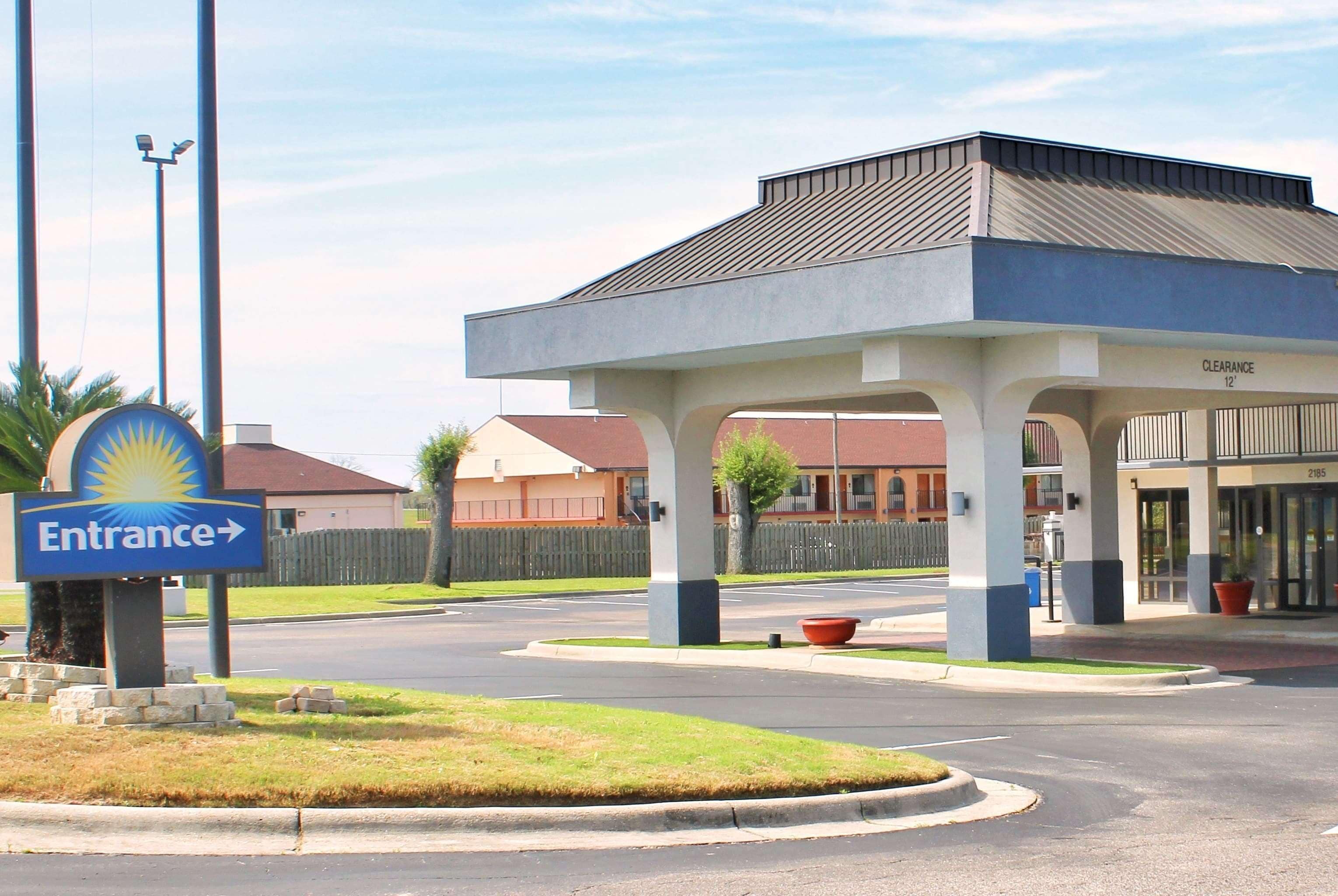 A hotel entrance with a clear sign, a covered waiting area, and a parking lot.