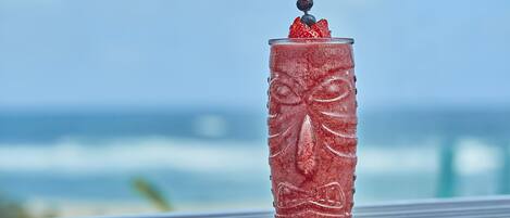 A glass with a textured design and a berry garnish on a metal surface with a blurred ocean and sky in the background.