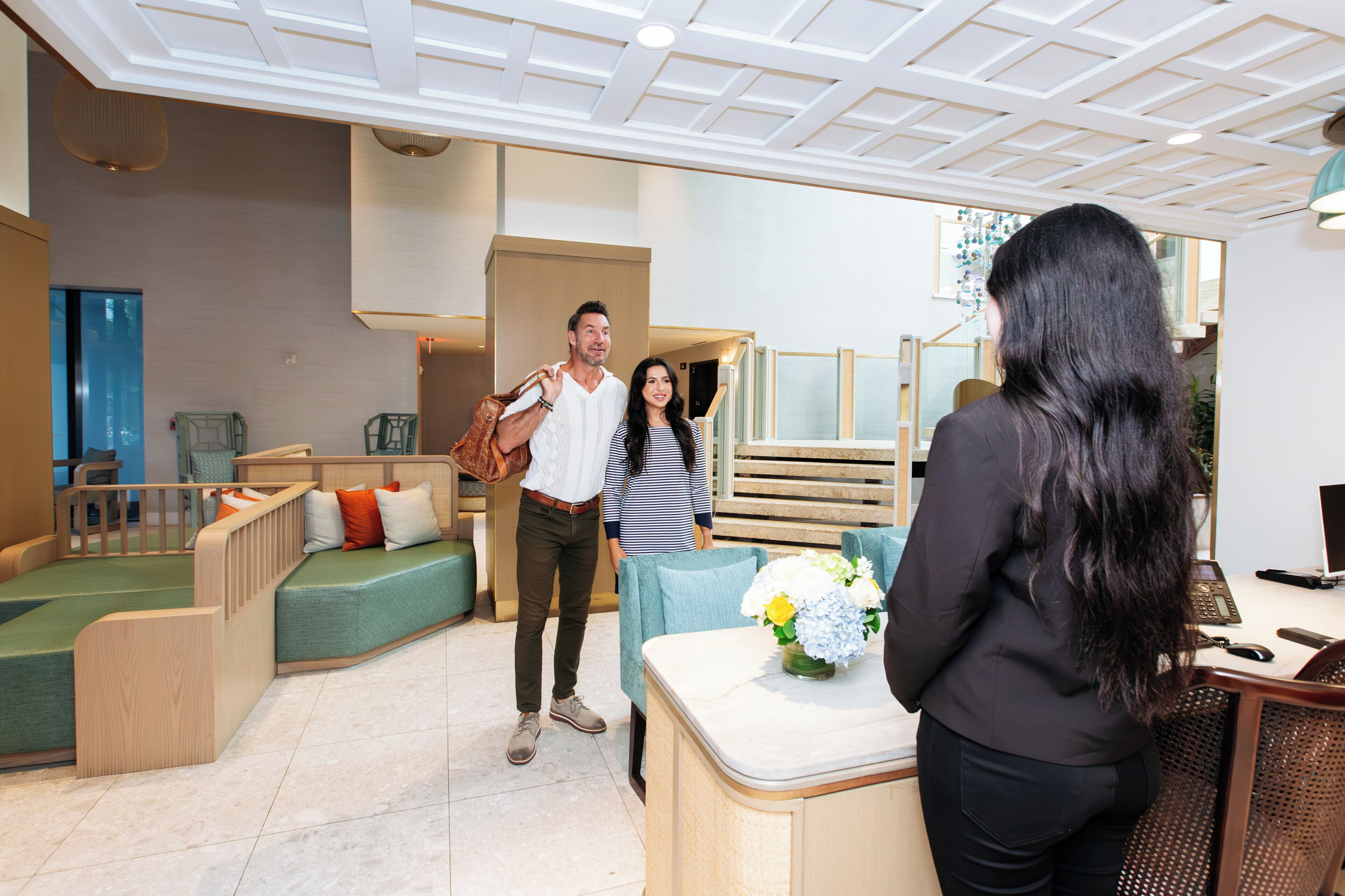 A modern hotel lobby with a seating area, a reception desk, and a staircase.