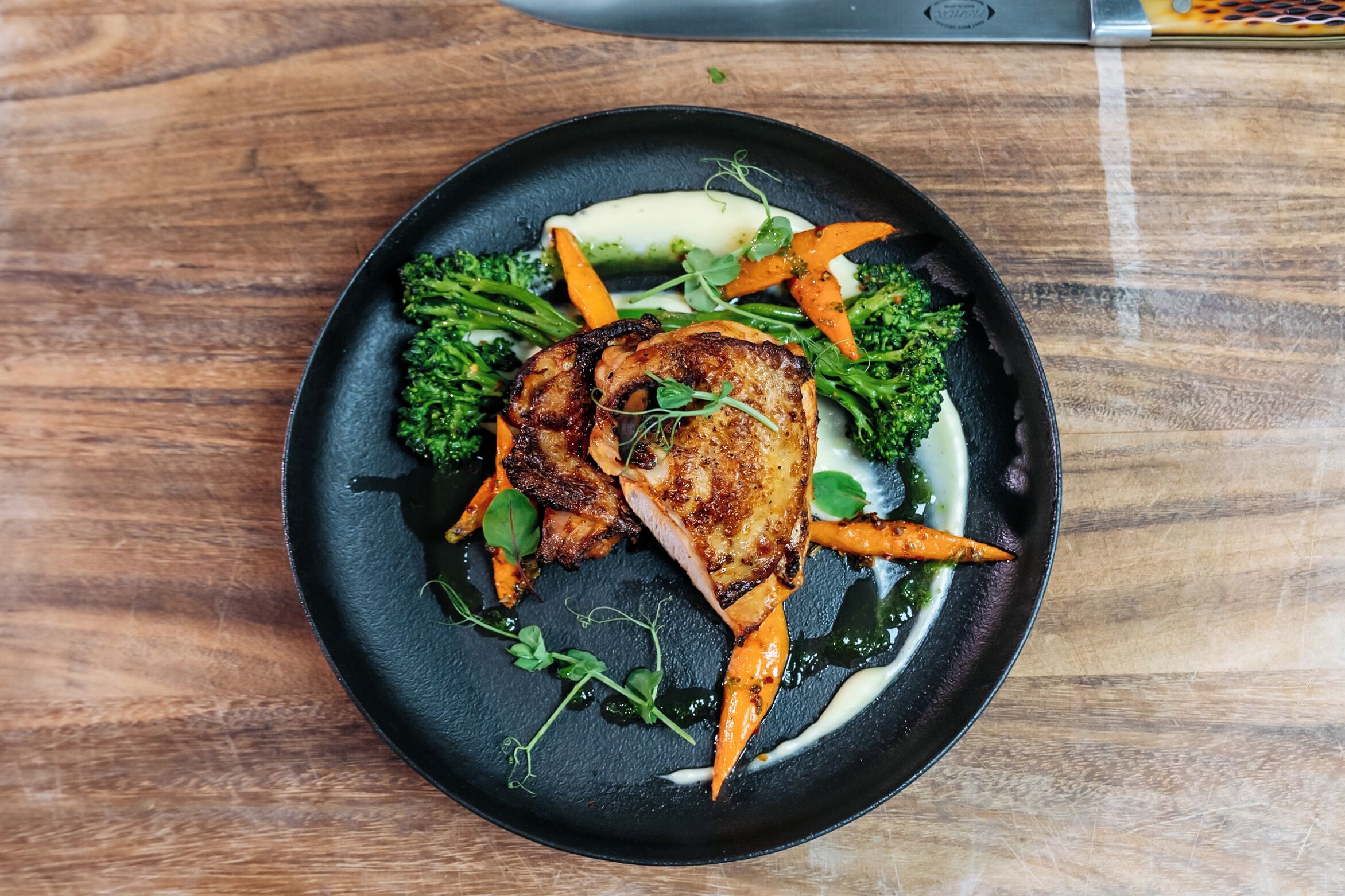 Ein Teller Essen mit Fleisch, Karotten und Brokkoli auf einer schwarzen Platte.