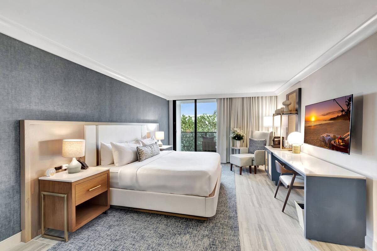 A modern hotel room with a large bed, a desk, and a TV.