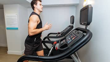 Un hombre corre en una cinta de correr en una habitación con un cartel de normas del gimnasio en la pared.