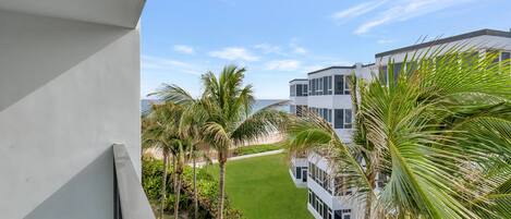 A modern building with a balcony overlooking a well-maintained lawn and palm trees.