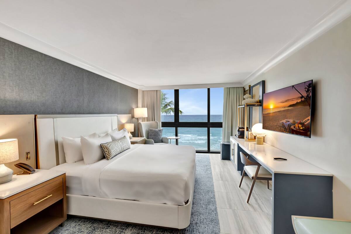 A hotel room with a large bed, bedside tables, a desk, and a view of the ocean.