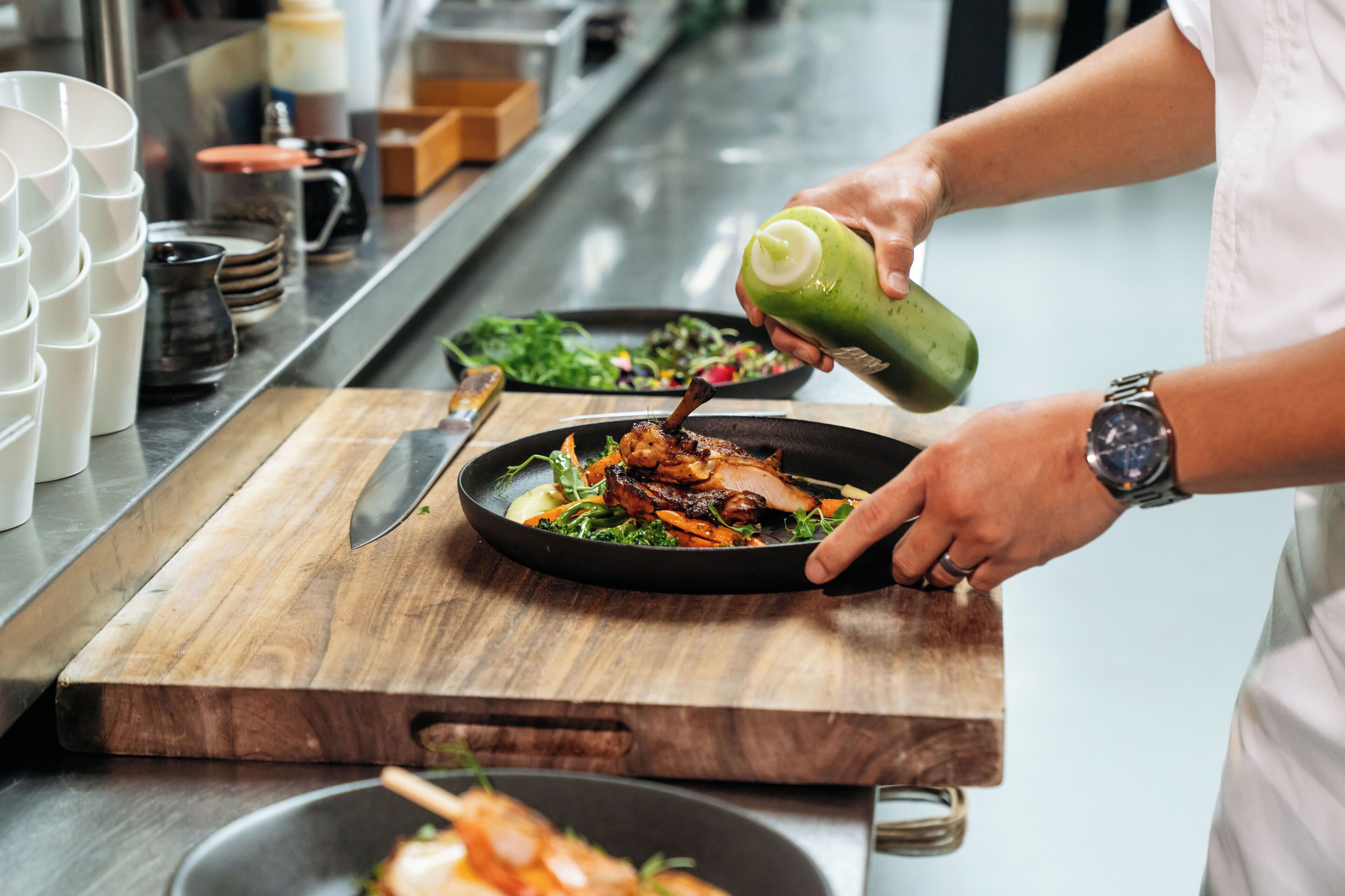 A chef pouring sauce onto a dish of food.