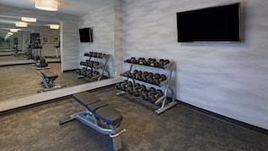 Un gimnasio con equipamiento de ejercicio, una banca y un estante con mancuernas.