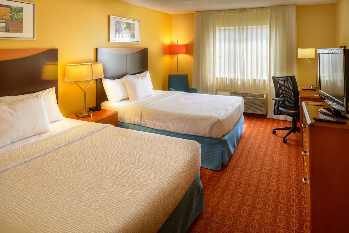 Une chambre d’hôtel avec deux lits, un bureau avec un ordinateur, une chaise et un téléviseur.