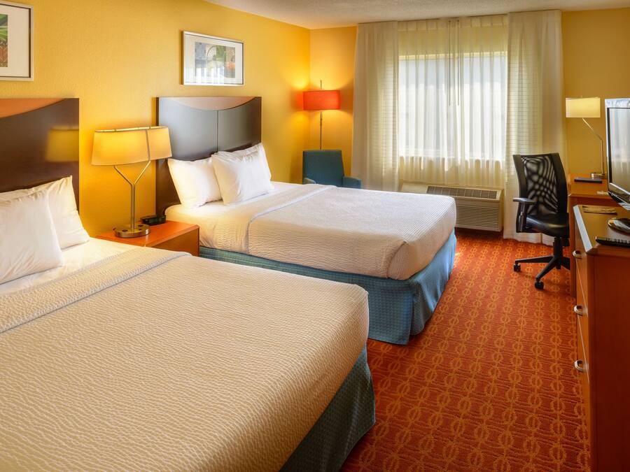 A hotel room with two beds, a desk with a computer, a chair, and a TV.