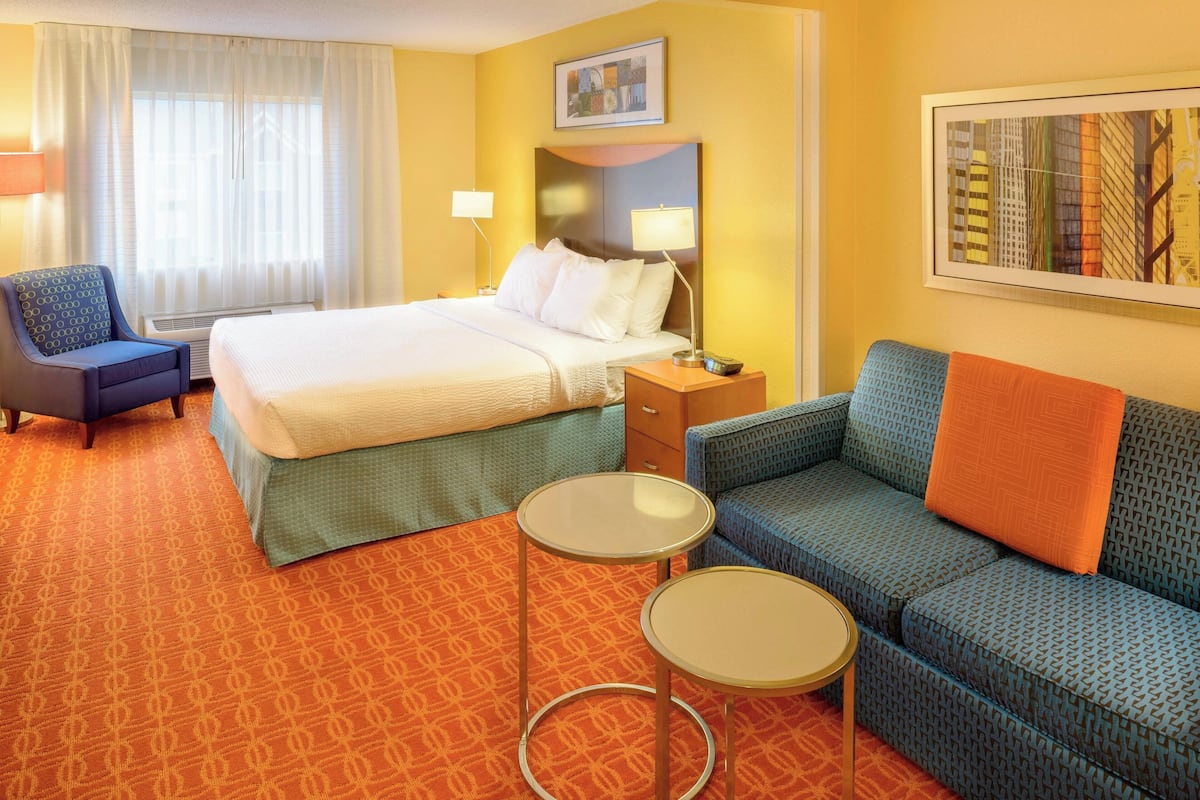 Une chambre d’hôtel avec un lit, deux tables de chevet, un canapé, une chaise et une fenêtre avec des rideaux.