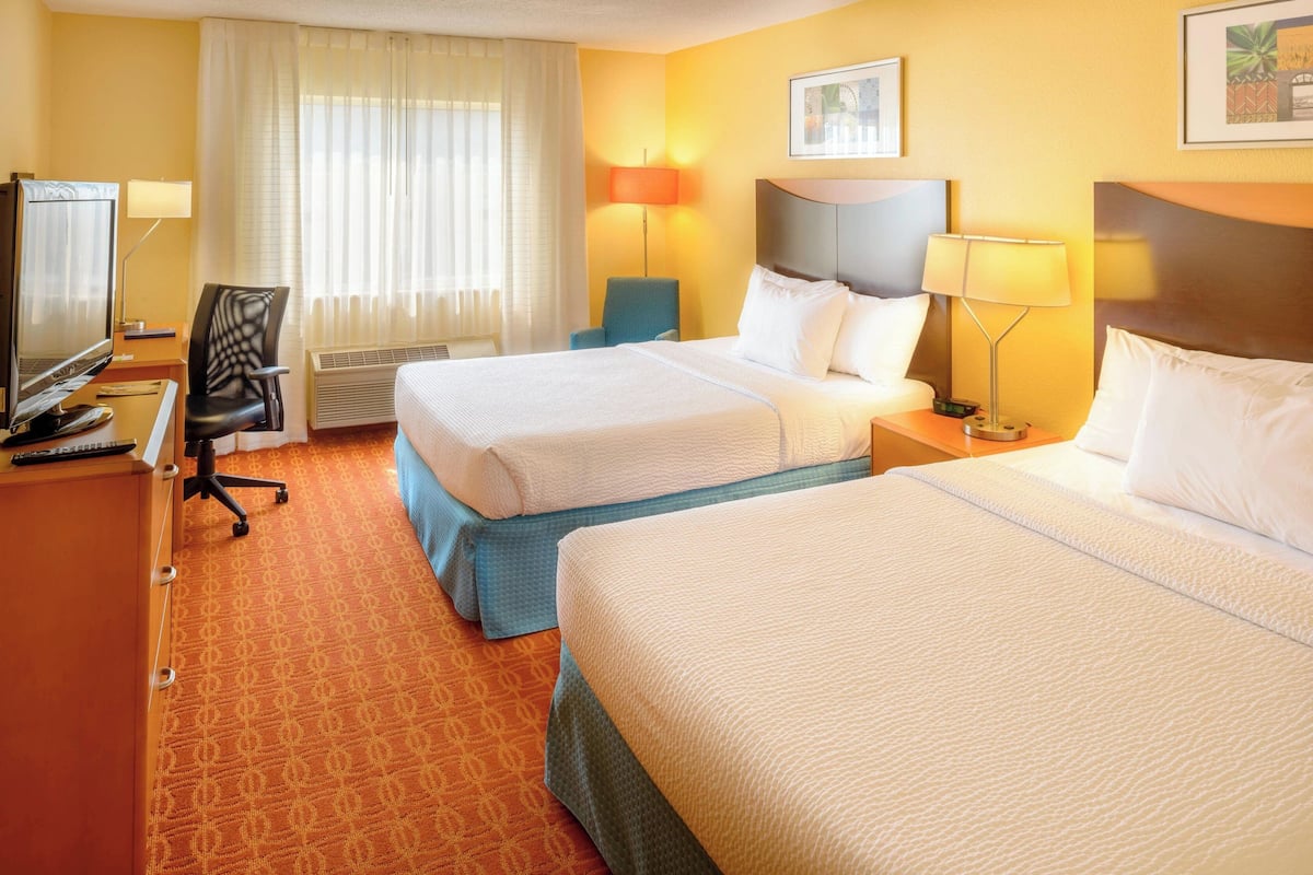 Une chambre d’hôtel avec deux lits, un bureau avec un ordinateur, une chaise et un téléviseur.