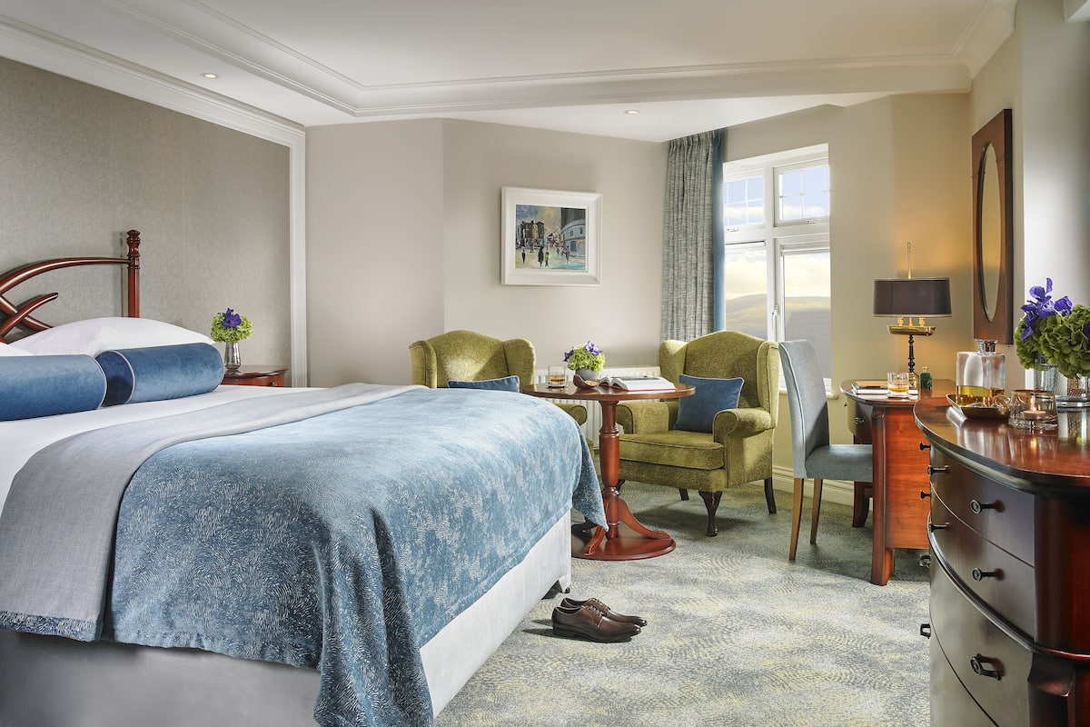 A hotel room with a large bed, two chairs, a desk, and a view of the outdoors.