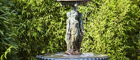 A fountain with a statue in the center, surrounded by lush green foliage.