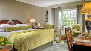 A hotel room with a large bed, a sitting area with a table and chairs, a lamp, and a view of the outdoors through a window.