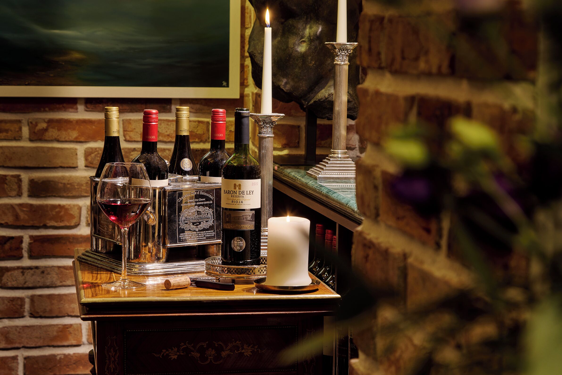 A bar area with bottles of wine, glasses, and a candle on a wooden counter.