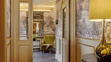 A hallway with a green armchair, a lamp, and a mirror.
