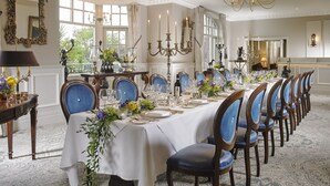 A formal dining room with a long table set for a meal, surrounded by blue upholstered chairs.