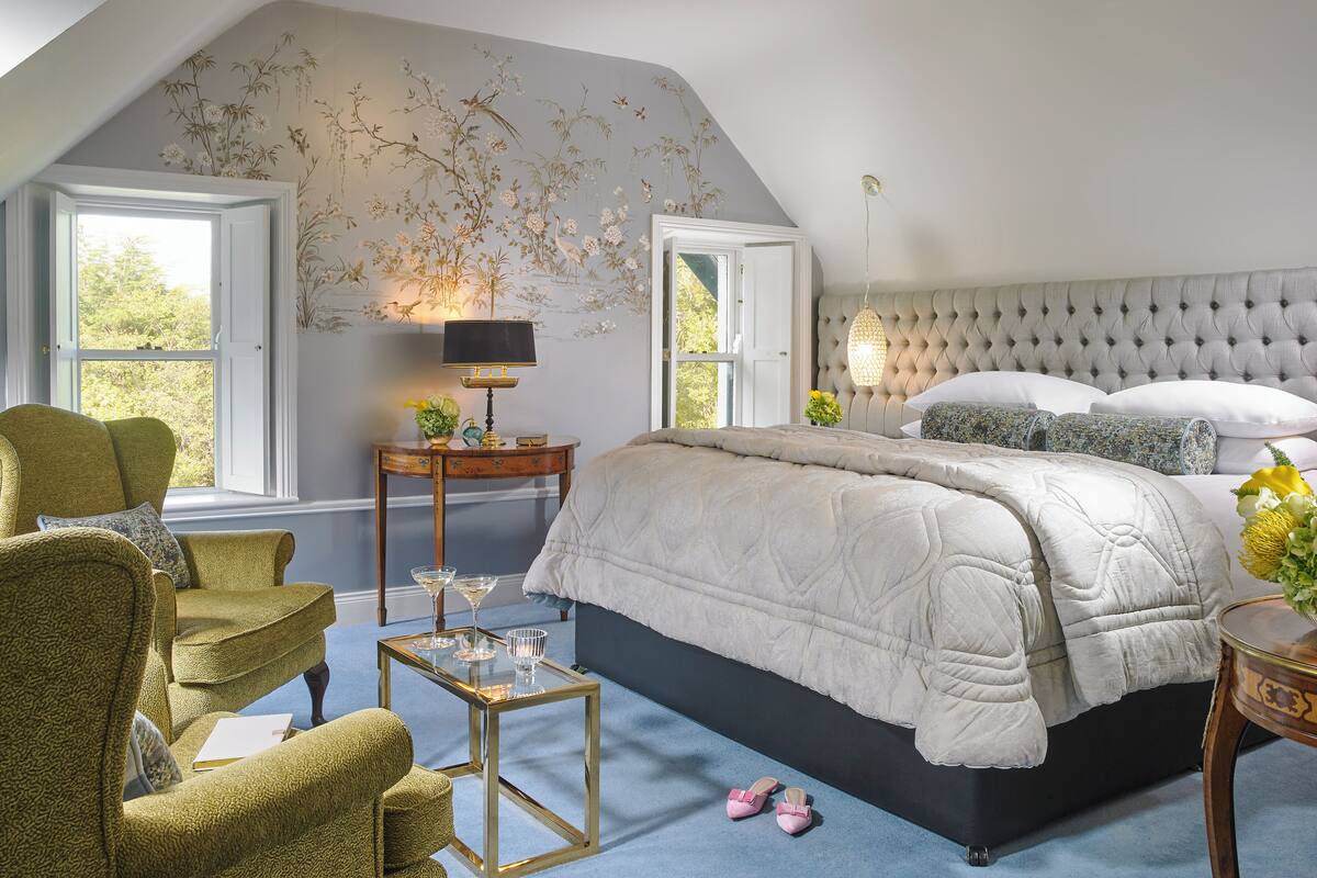 A bedroom with a large bed, a chair, a side table, and a lamp.