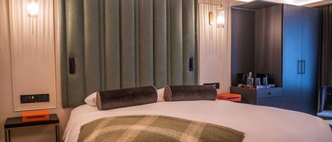 A hotel room with a large bed, a bedside table with a bowl, a nightstand, a TV, and a wardrobe.