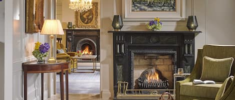 A traditional living room with a fireplace, a chandelier, and a green armchair.