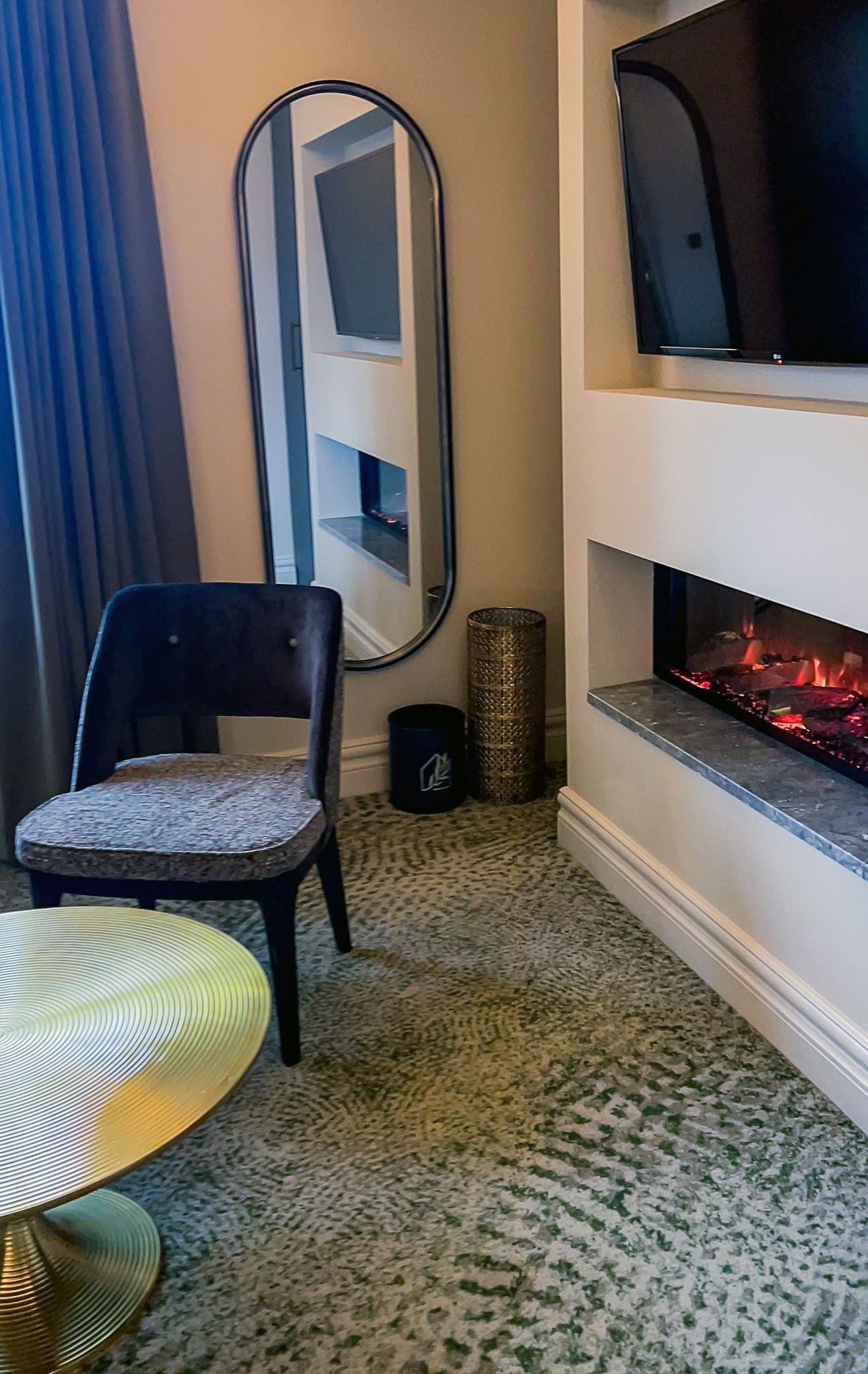 Ein Zimmer mit Kamin, einem Sessel, einem runden Tisch, einem Spiegel und einem Fernseher.