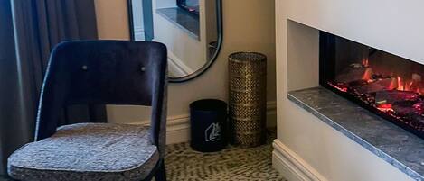 A room with a fireplace, a chair, a round table, a mirror, and a television.