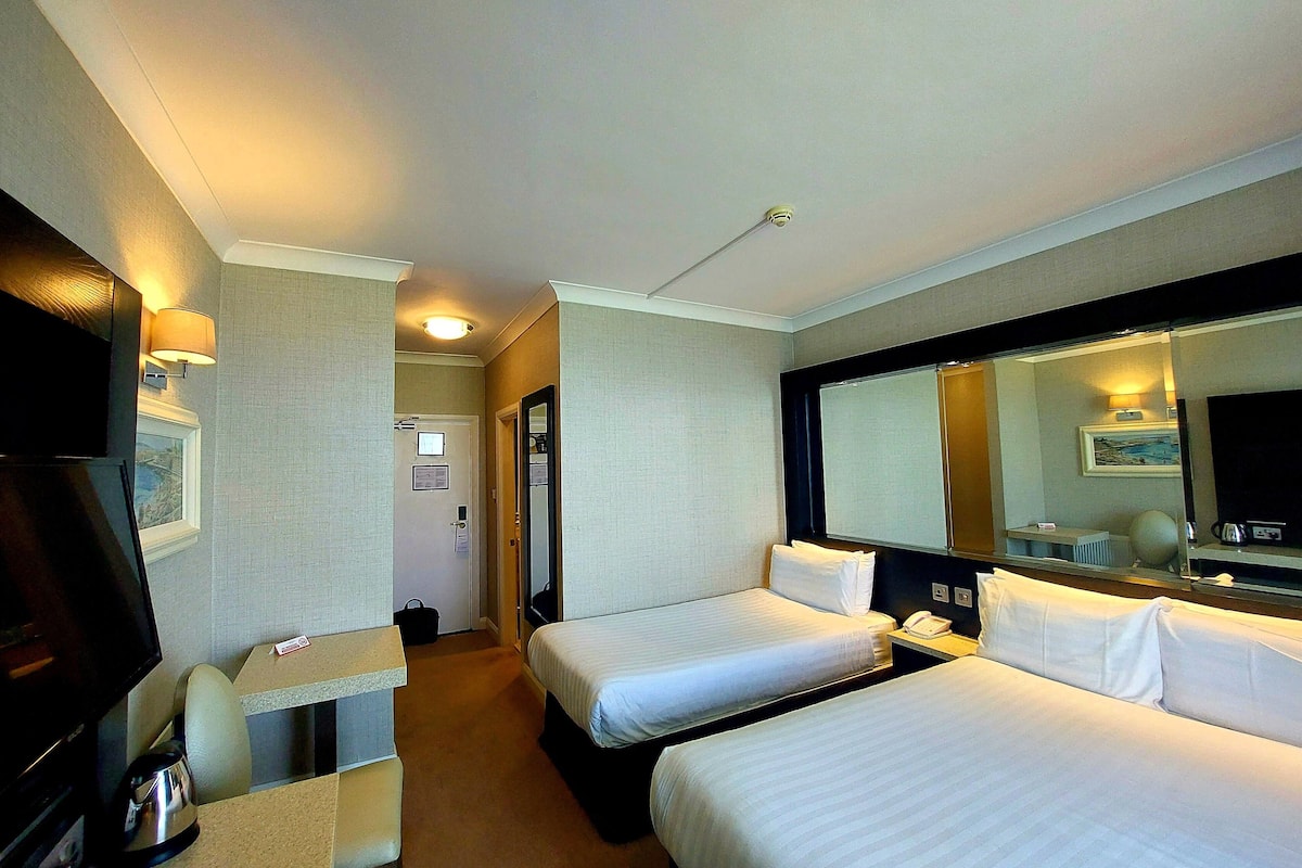 A hotel room with two beds, a desk with a chair, a television, and a large mirror.