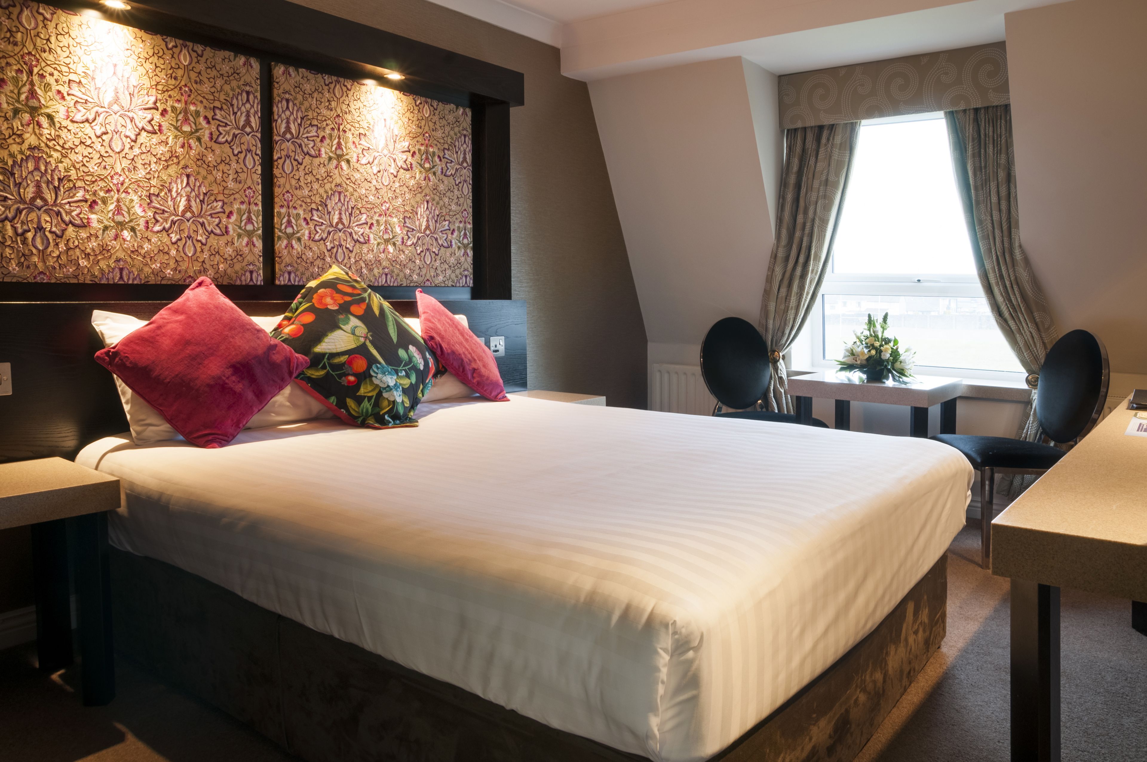 A hotel room with a large bed, a desk, and a view of the sea through the window.
