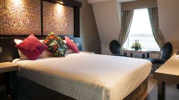 A hotel room with a large bed, a desk, and a view of the sea through the window.