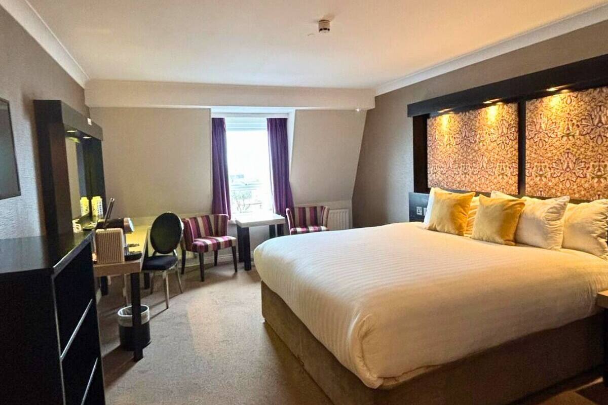 A hotel room with a large bed, a desk with a chair, a TV, and a window with curtains.