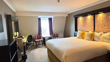 A hotel room with a large bed, a desk with a chair, a TV, and a window with curtains.