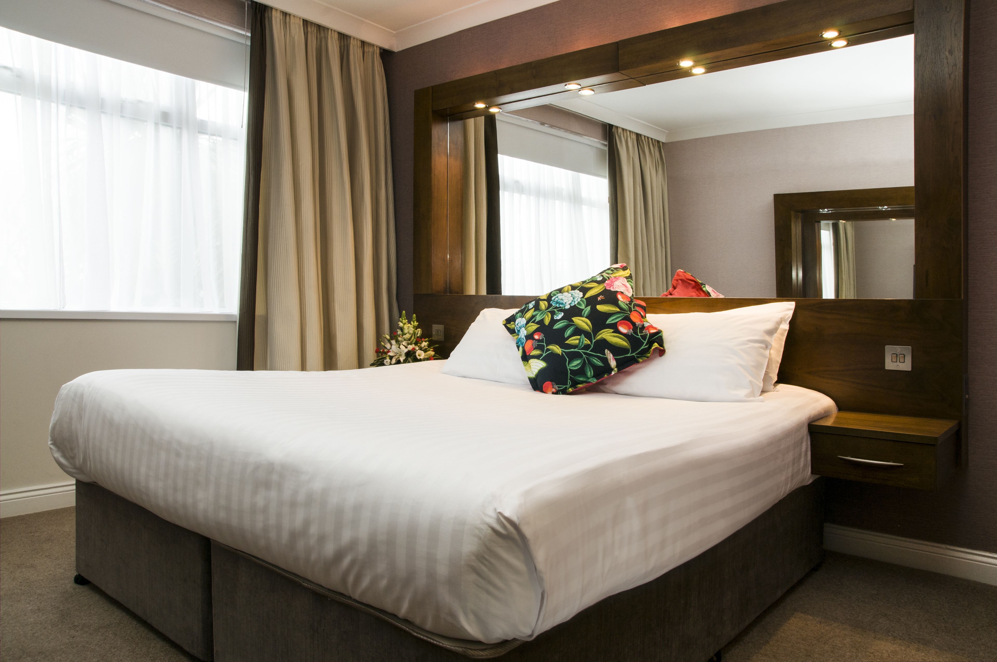 A neatly made bed with white linens, a floral pillow, and a wooden headboard.