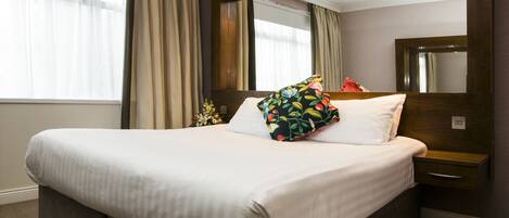 Una cama bien hecha con sábanas blancas, un cojín floral y un cabecero de madera.
