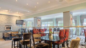A restaurant with a stone wall, multiple tables and chairs, and a fireplace.