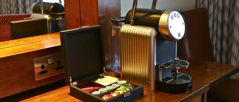 A compact espresso machine with a pull-down handle, a coffee grinder, and a box of assorted coffee pods on a wooden table.