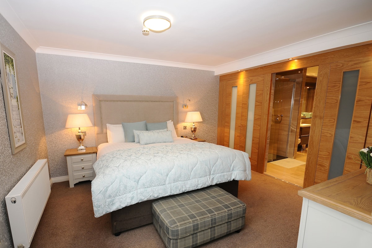 A bedroom with a large bed, bedside lamps, a radiator, a bench, and a wooden wardrobe.