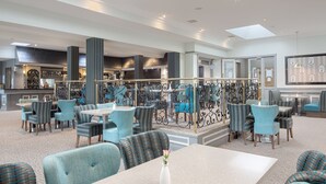 Un moderno hall de hotel con una amplia zona de estar, un bar central y vistas a la cocina.