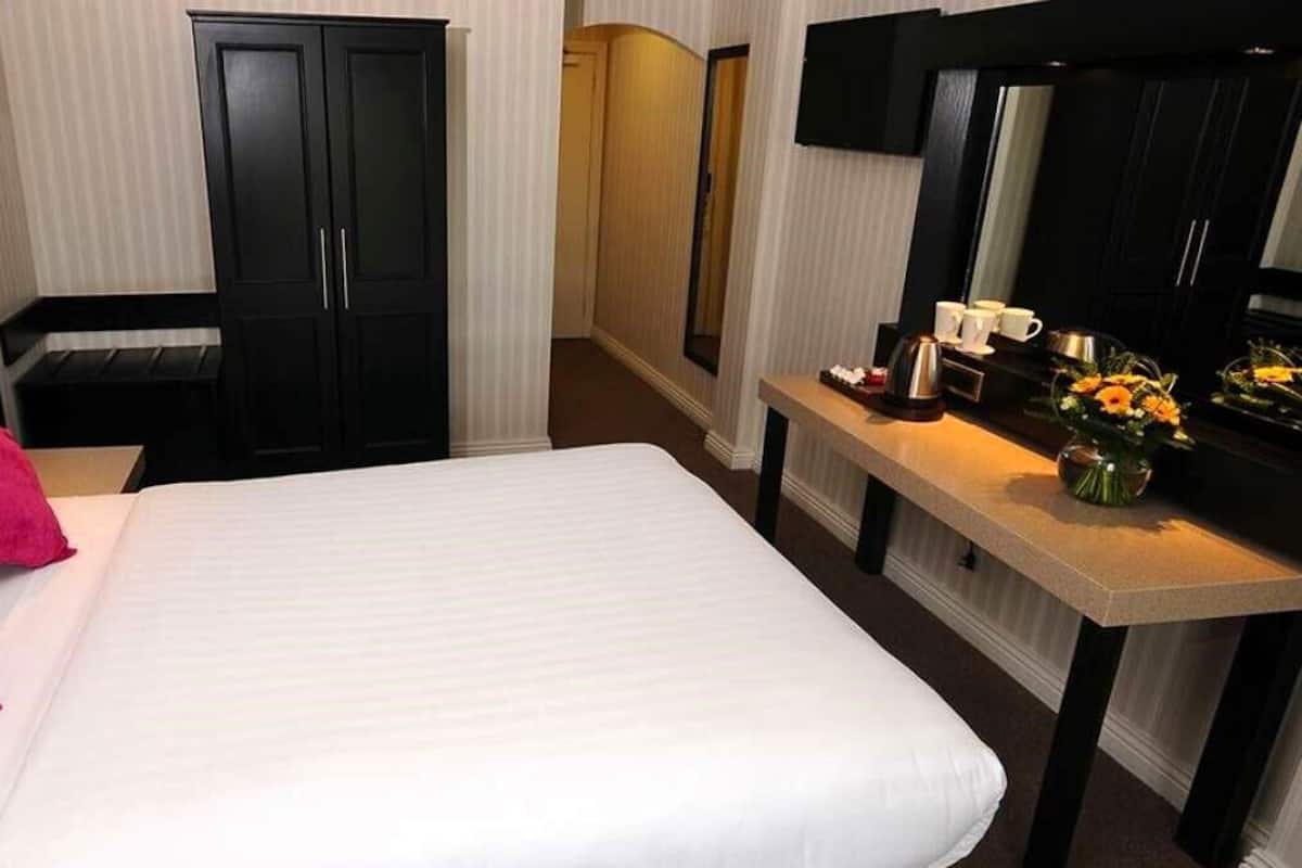 A hotel room with a large bed, a bedside table with a vase of flowers, a mirror, and a wardrobe.