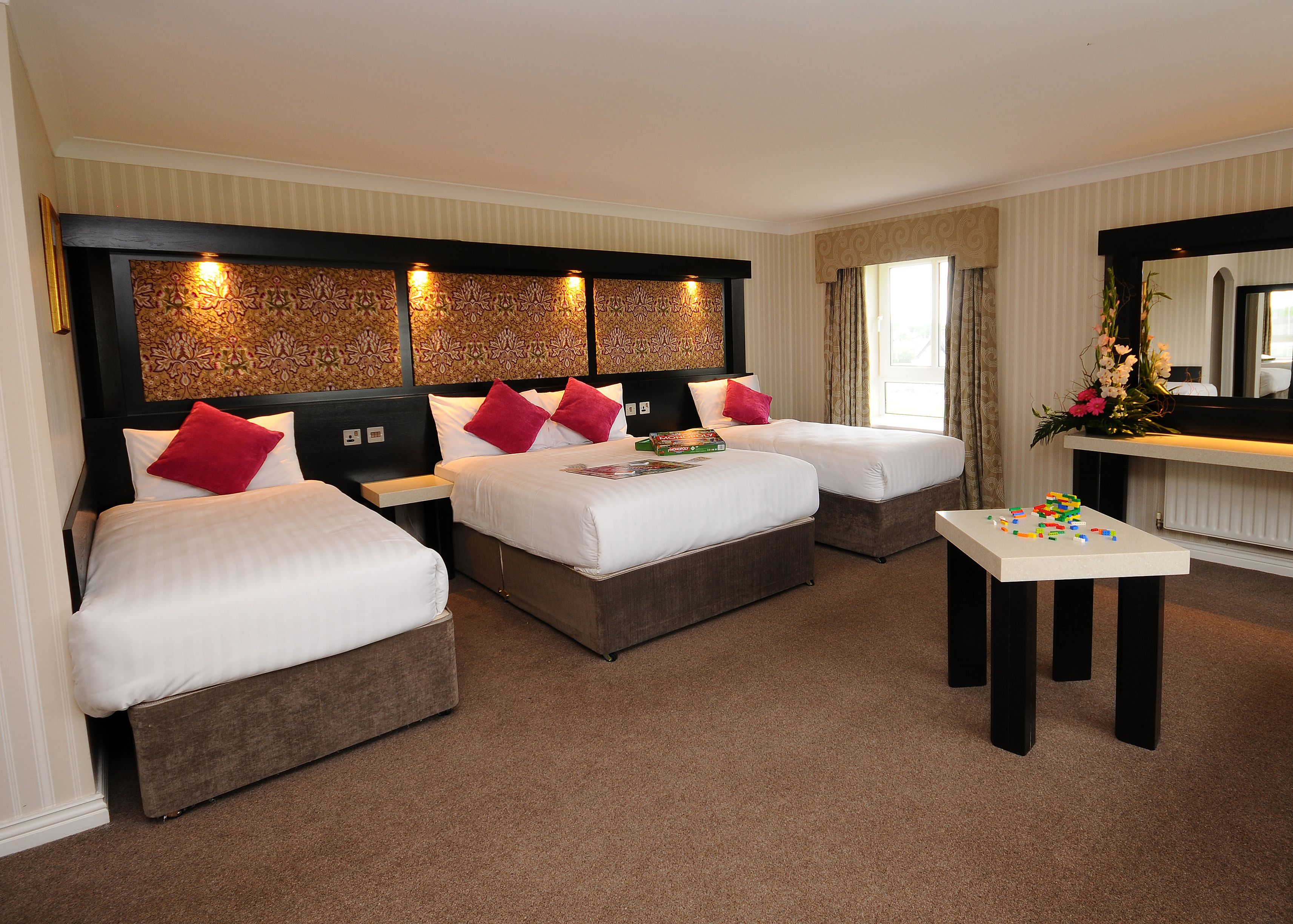 A hotel room with two beds, a small table, and a mirror.
