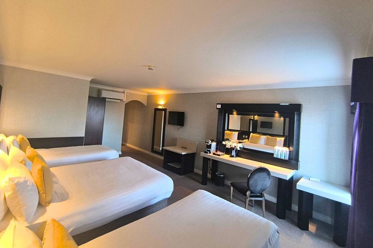 A hotel room with two beds, a desk with a mirror, a chair, and a small table.