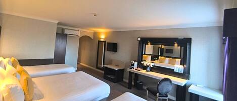 A hotel room with two beds, a desk with a mirror, a chair, and a small table.