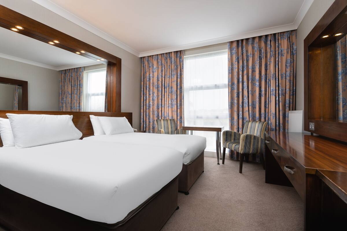 A hotel room with a large bed, a desk, a chair, and a window with curtains.