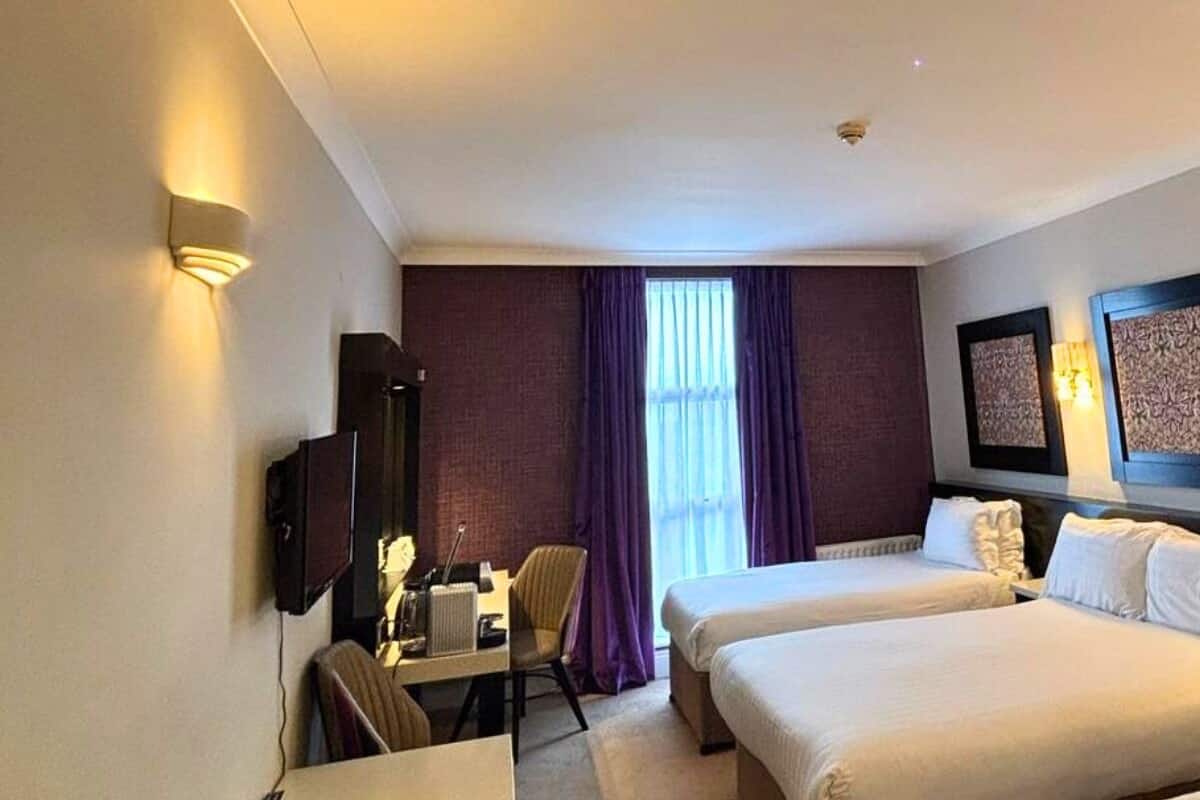 A hotel room with two beds, a desk, a chair, and a television.
