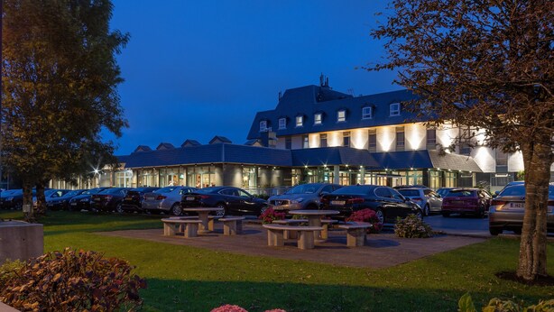 Un hotel con estacionamiento, mesas al aire libre y fachada bien iluminada.