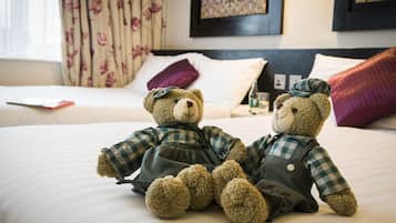 Dos ositos de peluche sobre una cama con cortinas florales y un cuadro en la pared.